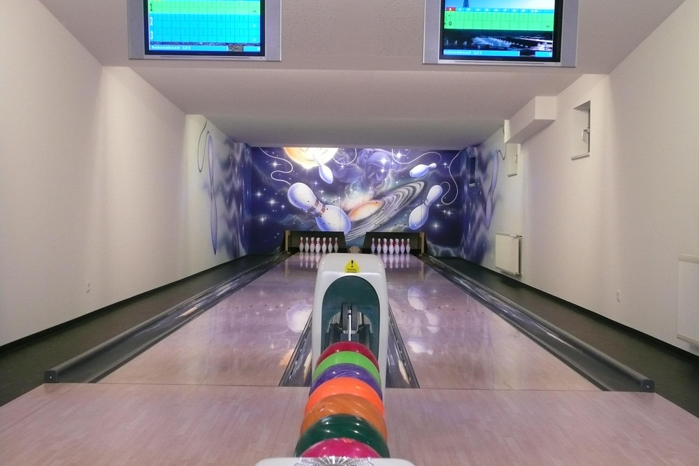 2 Bowlingbahnen mit Bowlingkugeln und 2 Monitore hängen von der Decke.