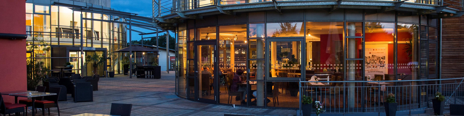 Restaurant von außen mit Terrassenbestuhlung, im dunkeln, von innen erleuchtet