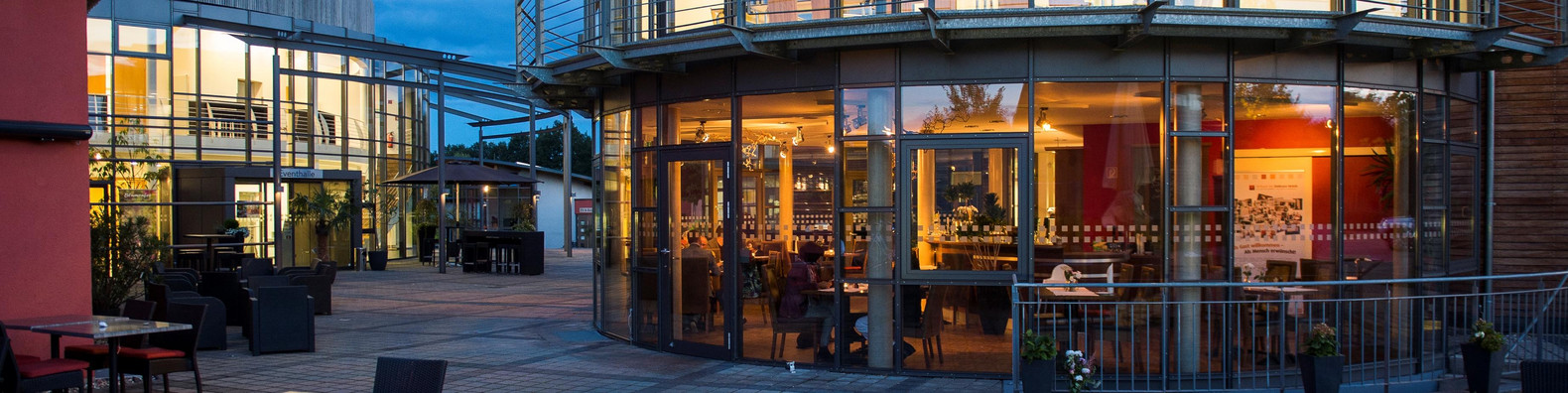 Restaurant von außen mit Terrassenbestuhlung, im dunkeln, von innen erleuchtet